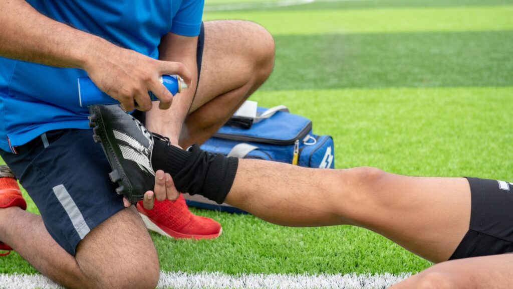 A sports trainer applying spray to a soccer player's ankle on a field