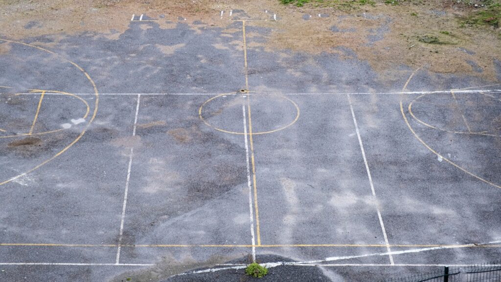 An abandoned, weathered basketball court with faded lines