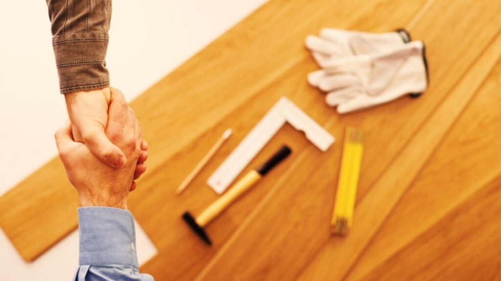 Two people shaking hands over a wooden surface with construction tools