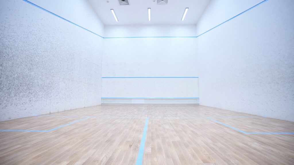Empty squash court with wooden floor and white walls