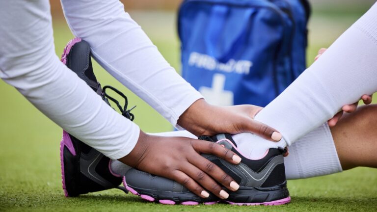 Person receiving first aid for an ankle injury with a visible first aid kit in the background