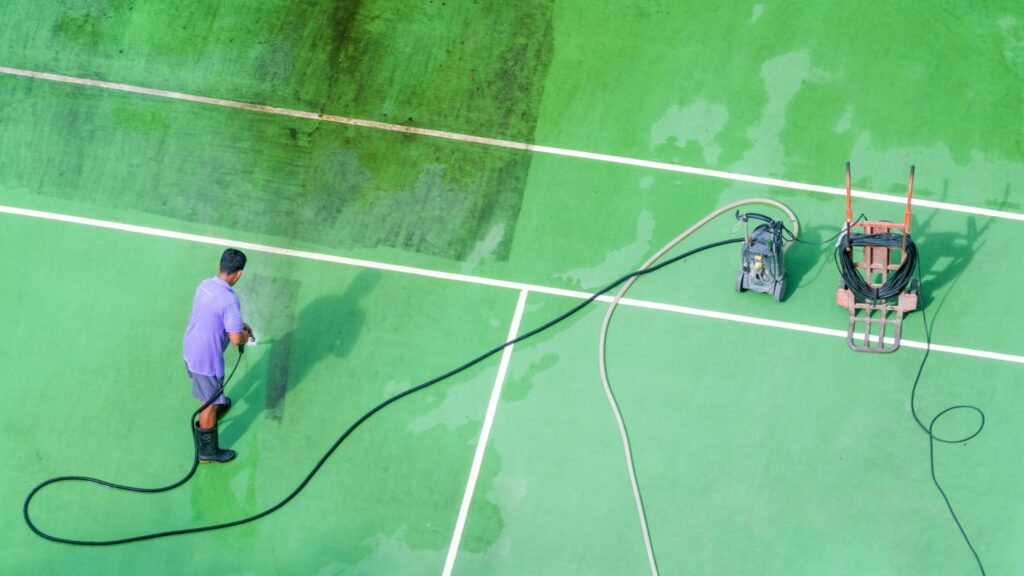 Person power washing a green tennis court