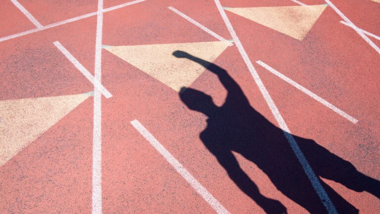 Shadow of a person raising their arm on a running track
